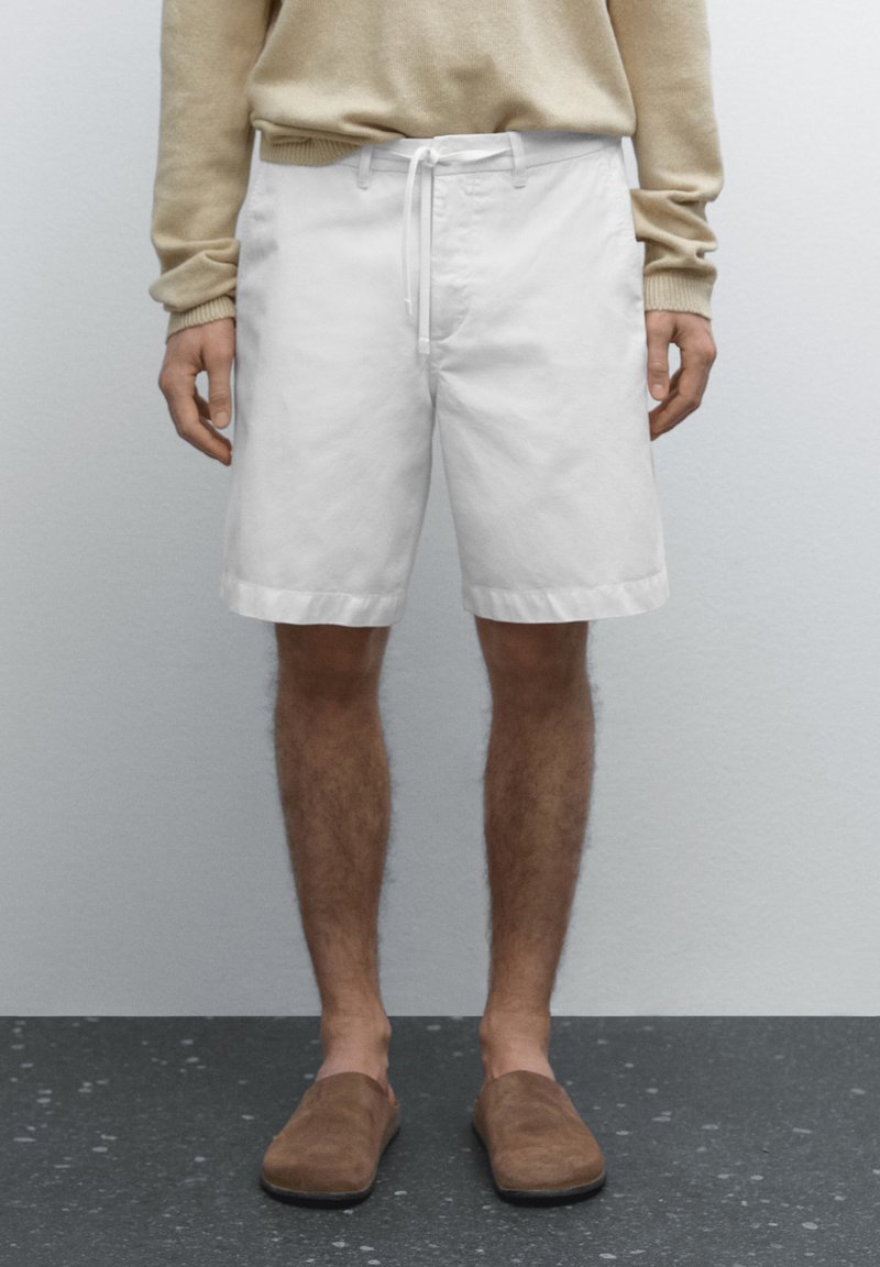 Hvide bomuldsshorts med en snor i taljen, med lige snit og opsmøgte kanter, parret med brune slip-on sko.