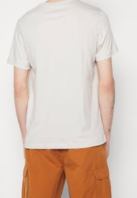 Beige bomullströja med rund hals och korta ärmar, visad bakifrån. Slät textur, avslappnad passform, inga synliga logotyper eller mönster.