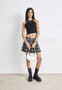 Black cropped halter top, plaid mini skirt, and chunky black ankle boots. Holding a small white handbag with a curved shape.