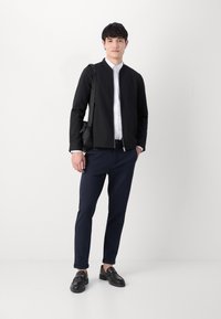 Μαύρο bomber jacket, άσπρο πουκάμισο με γιακά, ναυτικές παντελόνες και μαύρες εσπαντρίλες με χρυσές λεπτομέρειες, όλα σε λευκό φόντο.