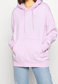 Felpa con cappuccio di colore viola chiaro, dotata di tasca a marsupio, cordini e polsini a costine. Vestibilità ampia con superficie in tessuto liscia.