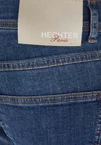 Dark blue denim jeans featuring a visible label reading "HECHTER Paris." Includes orange stitching and two back pockets.