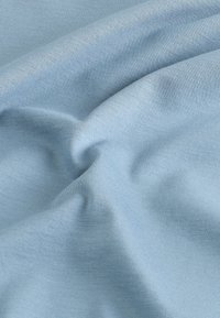 Lichtblauwe katoenen stof met een gladde textuur, voorzien van subtiele diagonale ribbels en zachte plooien die zachte schaduwen creëren.