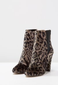 Par de botines de tacón alto con tela de estampado de leopardo marrón y negro y paneles laterales elásticos negros sobre una superficie blanca.