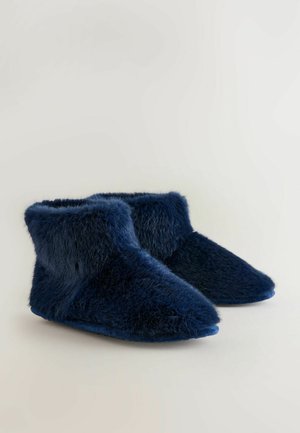 Stivaletti alla caviglia in pelliccia sintetica di un blu navy, con una texture morbida, punta affusolata e bordo superiore arrotondato. La suola è liscia e leggermente curvata.