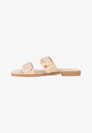 Sandalias descalzas con dos correas anchas, adornadas con tachuelas doradas y acentos circulares, con una suela de goma plana y textura suave.