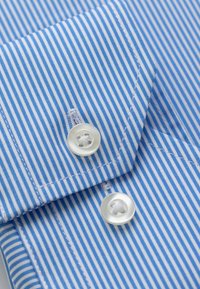 Blauw-witte gestreepte overhemdenkraag met ronde randen, voorzien van twee witte knopen en zichtbare stikdetails. Zacht katoenmateriaal.