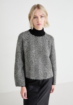 Maglione a maglia con motivo a spina di pesce bianco e nero, con collo alto a coste nere. Taglio morbido, maniche lunghe e orlo corto.