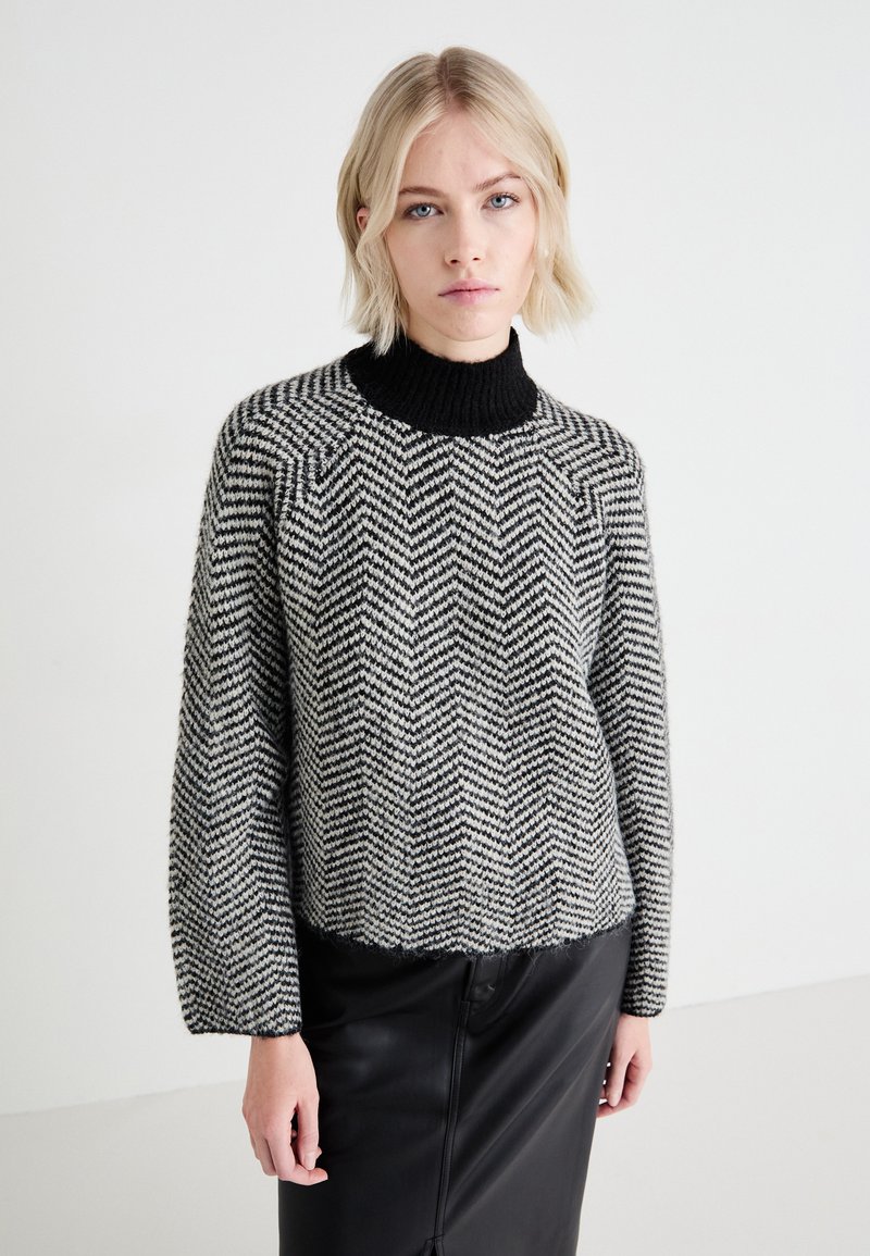 Maglione a maglia con motivo a spina di pesce bianco e nero, con collo alto a coste nere. Taglio morbido, maniche lunghe e orlo corto.