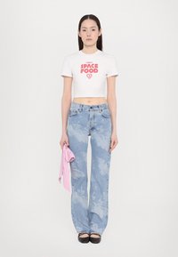 White cropped t-shirt with red "SPACE FOOD" graphic, paired with light blue flared jeans featuring cloud-like patterns. Holding a pink accessory.