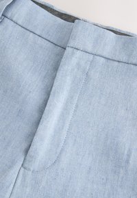 Light blue denim pants waistband with visible seam and button closure area on a plain background.