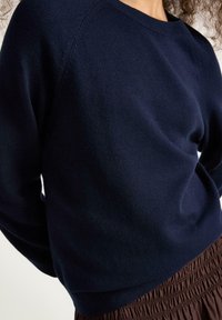 Mörk marinblå tröja med rundad halsringning, raglanärmar och mjuk stickad textur, tillsammans med en brun smockad kjol.