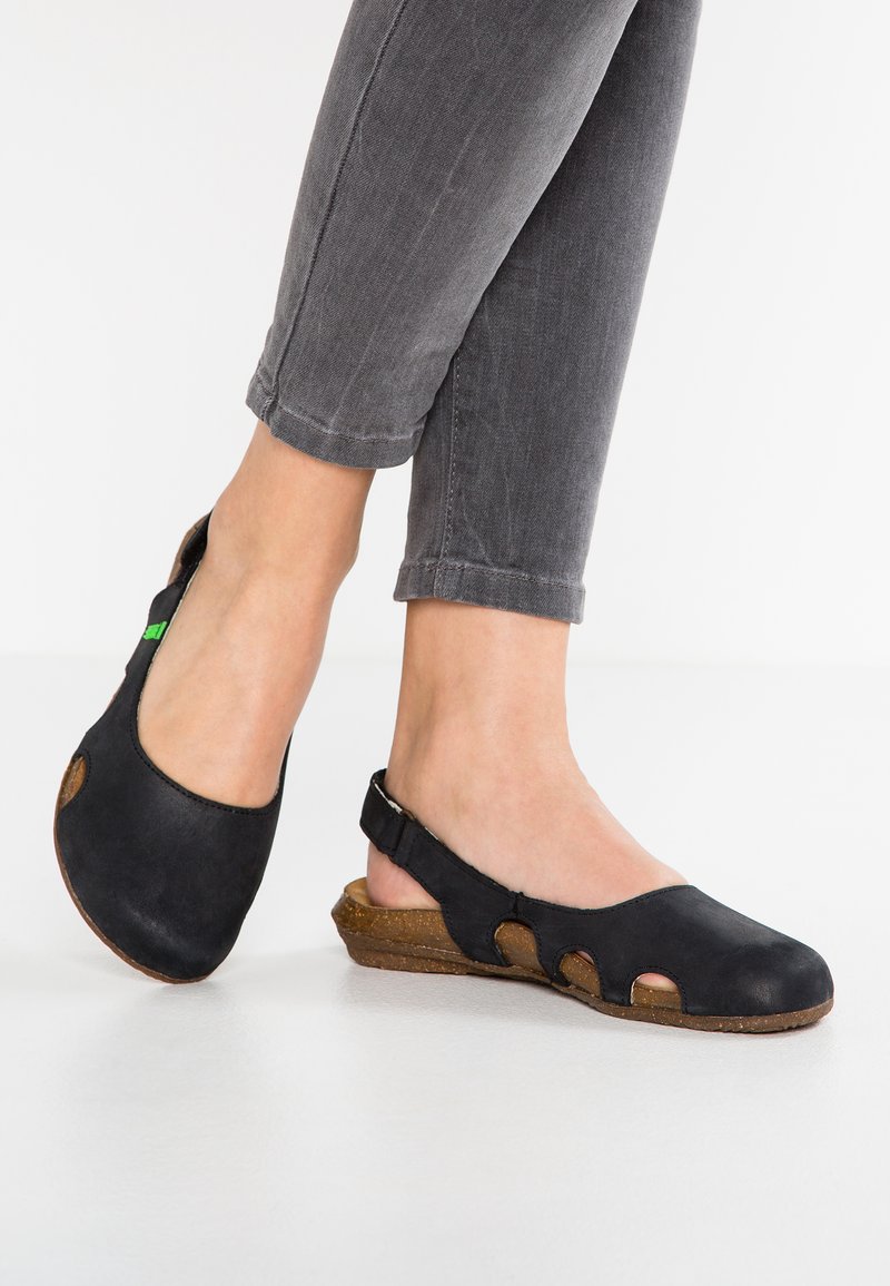 Bottines en suède noir avec des découpes, semelle en liège basse et texture douce. Portées avec un jean gris retroussé.