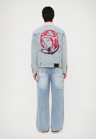 Veste en denim bleu clair avec un graphisme d'astronaute rouge au dos, associée à un jean bleu clair à jambes larges avec deux poches avant.