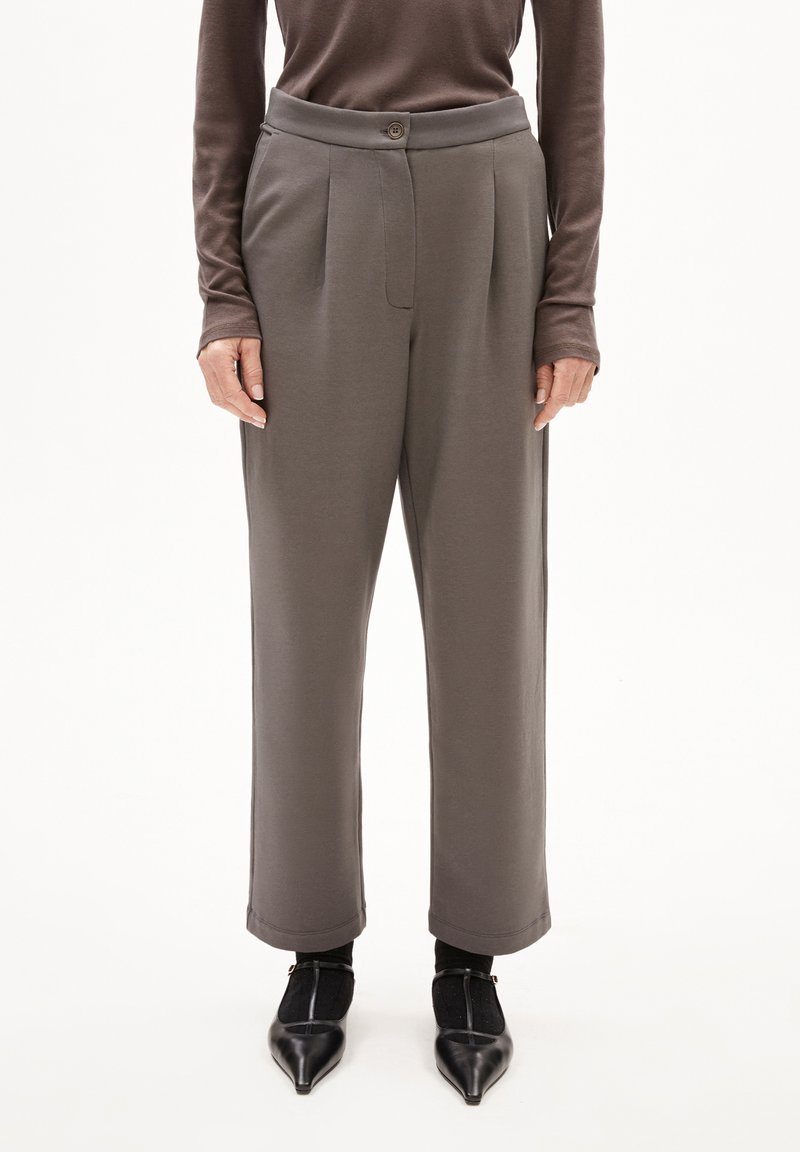 Grijze, hoge taille broek met een geplooid voorkantontwerp, een soepele textuur en een kleine knoopsluiting, gecombineerd met zwarte puntige schoenen.