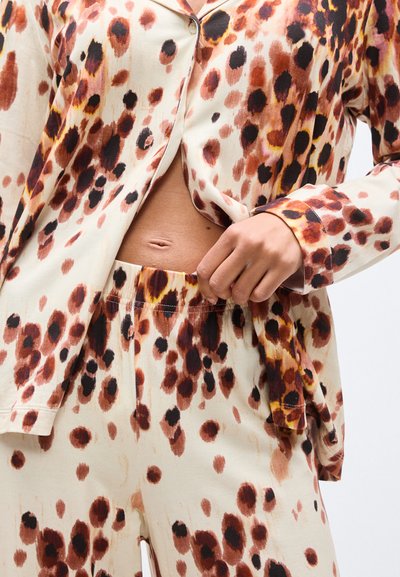 Κοντινό πλάνο ενός ατόμου που φοράει πουκάμισο και παντελόνι με λεοπάρ σχέδιο, με το χέρι να ρυθμίζει τη λάστιχη μέση, αφήνοντας ακάλυπτη την κοιλιά.