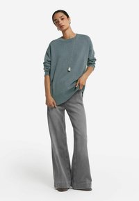 Helles türkisfarbenes Strickpullover mit geripptem Saum, kombiniert mit hoch taillierten, ausladenden grauen Jeans. Lange Ärmel und eine lässige Passform; minimale Accessoires inklusive.