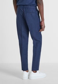 Marineblauwe linnen broek met een relaxed fit, met een tailleband, twee achterknopen en zijzakken, gecombineerd met witte sneakers.