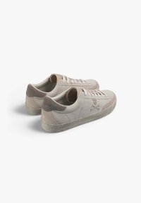 Par de zapatillas de ante beige con suelas de goma texturizadas, cierres con cordones en la parte delantera y un logo de calavera y huesos cruzados en el lado visible.