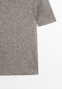 T-shirt en maille grise à manches courtes, présenté de la taille à la manche, avec une texture douce légèrement chinée sur fond blanc.