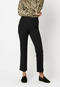 Czarne spodnie o prostym kroju, z kieszeniami z przodu i gładką teksturą, zestawione z beżową bluzką w kropki oraz ciemnymi butami.