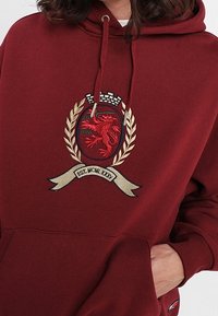 Felpa bordeaux con tasca a marsupio, caratterizzata da un crest ricamato con un leone rosso, rami di alloro e un banner sottostante.