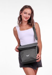 Šedá rolovací taška vyrobená z odolného materiálu, s logem na přední straně, nastavitelným popruhem a elegantním, moderním designem.