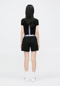 Top negru cu mâneci scurte și logo mov pe spate, asortat cu șorturi negre și adidași albi. Design simplu, potrivit, material din bumbac.