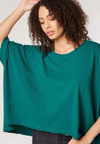 Türkisfarbenes Oversized-T-Shirt aus leichtem Stoff, mit rundem Halsausschnitt und kurzen Ärmeln, entspannter Passform und glatter Textur.