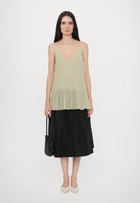Light green, pleated chiffon top with V-neck, layered hem. Black, knee-length skirt. Light-colored, pointed flats. Woven bag on shoulder.