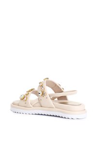Beige sandals with cross straps, adorned with various decorative jewels. Thick white sole with a zigzag pattern. Soft texture, lightweight design.