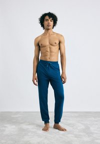 Heren blauwe joggerbroek van zacht materiaal, met een elastische tailleband met trekkoord, taps toelopende boorden en een gladde textuur.