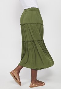 Falda verde oliva hasta la rodilla hecha de tela ligera. Presenta volantes en capas, cintura elástica y una silueta fluida.