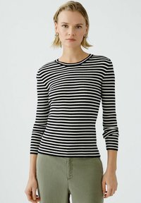 Haut à manches longues rayé noir et blanc en côtes, avec un col rond, présentant un design ajusté et un tissu texturé. Associé à un pantalon vert.
