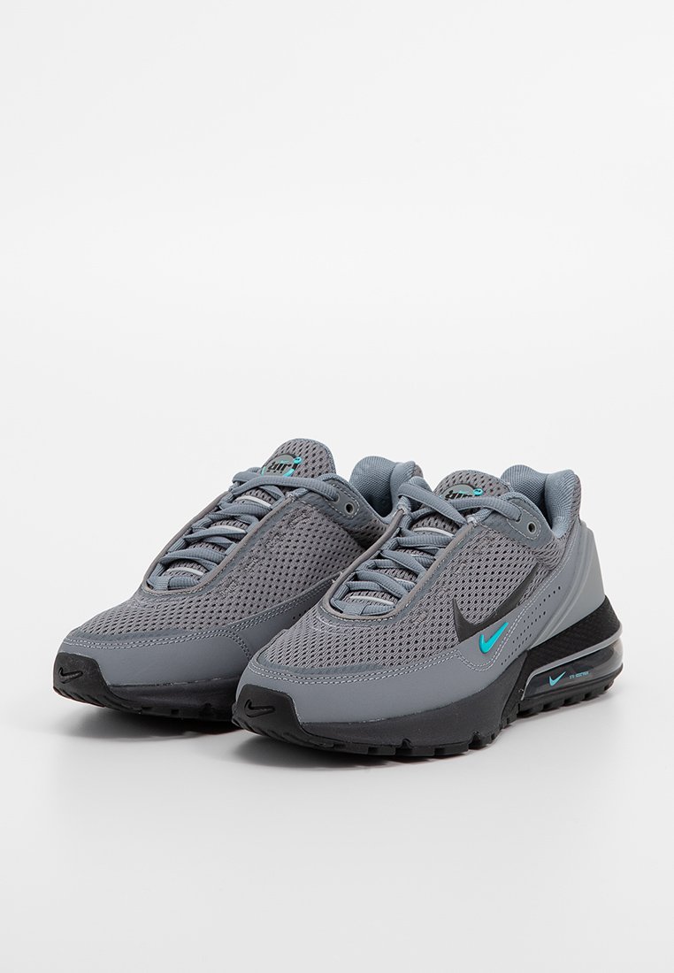 Zapatillas de running Nike en gris con parte superior de malla, suela de goma negra y acentos turquesa. Presentan un diseño de cordones para un ajuste seguro.