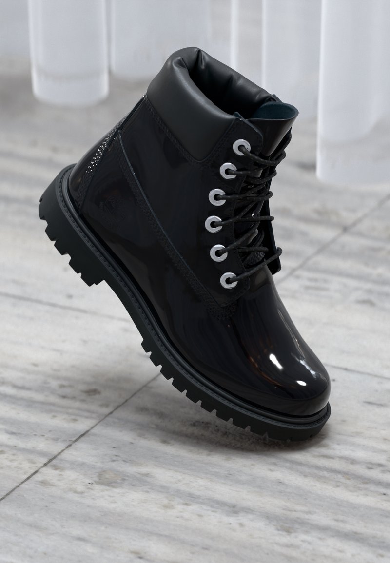 Botte cheville en cuir noir brillant avec semelle à gros crampons et col rembourré, positionnée sur un sol carrelé clair.