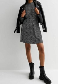 Svart klänning med vita prickar, med en figursydd överdel och en utsvängd kjol. I kombination med en svart läderjacka. Kraftiga svarta stövlar i ankellängd fulländar looken.