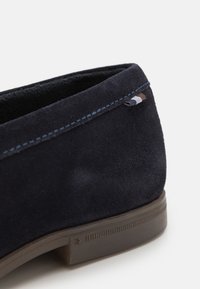 Pantof navy din suede cu o finisare texturată, talpă plată din cauciuc maron, și cusături albastre subtile cu un accent colorat aproape de toc.