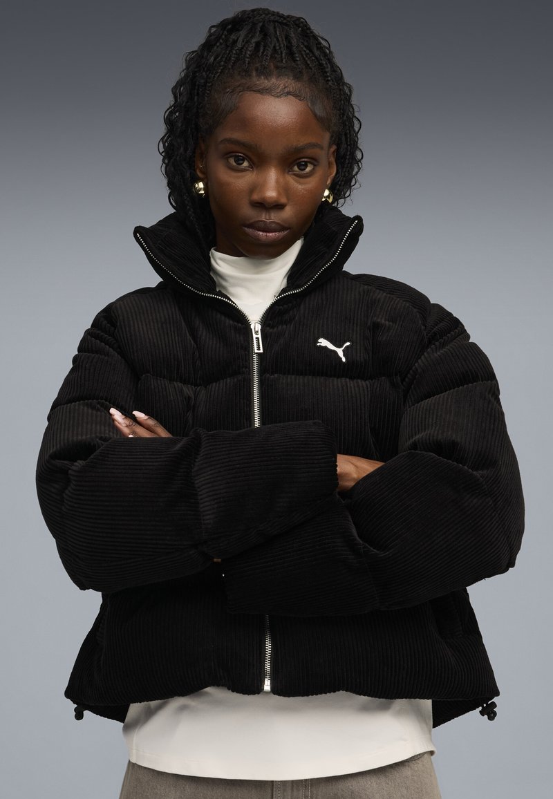 Giacca puffer nera in velluto con alto colletto, chiusura con zip e logo Puma bianco. Presenta un motivo testurizzato, una vestibilità oversized e polsini elastici.