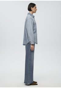 Light blue denim shirt with long sleeves and pocket, paired with matching high-waisted straight-leg jeans. Brown pointed shoes.