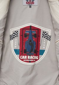 Lichtgrijs textiel met een grafisch ontwerp van een blauwe raceauto binnen een rood schild. Inclusief geruite vlaggen en tekst: "CAR RACING INTERNATIONAL CUP."