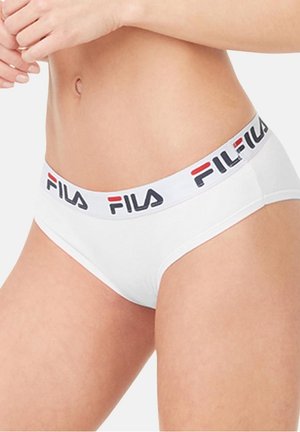 Femme portant un slip blanc de marque FILA avec une taille haute, montrant la section médiane et le haut des cuisses sur un fond uni.