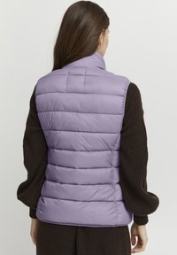 Lila puffer gilet met horizontaal doorstikte patronen en een hoge kraag. Lichtgewicht stof en licht gepolsterd voor warmte.