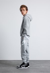 Šedá mikina s klokankou, spárovaná s odpovídajícími tepláky s bílým logem Nike. Černé a šedé vysoké tenisky.