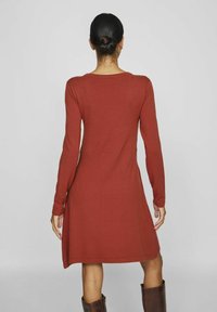 Robe à manches longues couleur rouille avec un ourlet évasé, fabriquée en tissu doux. Présente un décolleté rond et un design de dos sans couture.