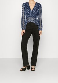 Blusa a fantasia blu navy con maniche lunghe trasparenti, vita sfiancata e scollo a V, abbinata a jeans neri a gamba dritta e sandali neri con zeppa.