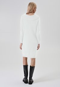 Abito bianco lavorato a maglia con ampio colletto, maniche lunghe e taglio aderente, abbinato a stivali neri alti con finitura testurizzata.