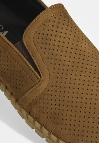 Brauner perforierter Lederschuh zum Hineinschlüpfen mit elastischen seitlichen Akzenten und einer kontrastierenden Gummisohle. Die Oberfläche hat eine strukturierte Haptik.