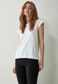 Camiseta blanca de manga corta con tejido texturizado, escote redondo y un corte relajado. Combinada con pantalones negros.