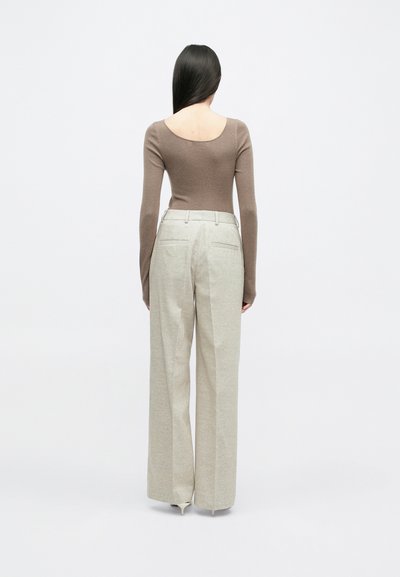 Smeđi pripijeni dugi rukav s širokim izrezom, uparen s hlačama visokog struka širokih nogavica od svijetle bež boje u teksturiranom materijalu.